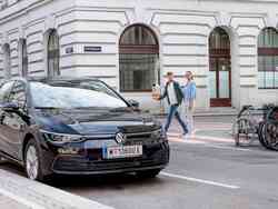 Ein Mann und eine Frau gehen hinter einem schwarzen VW-Golf über die Straße Ein Mann und eine Frau gehen hinter einem schwarzen VW-Golf über die Straße